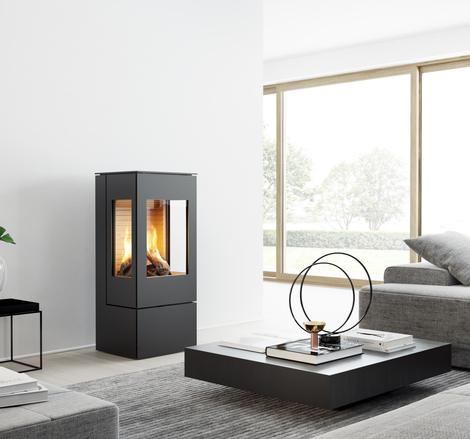 Stufa a gas NEXO 100 in nero con porta in acciaio e due finestre laterali in un soggiorno moderno e luminoso