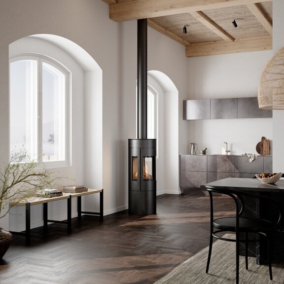 Stufa a gas VIVA 120 L in nero con porta in acciaio e finestra laterale in una cucina con tavolo da pranzo in stile nordico