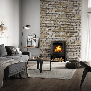 Stufa a legna Q-TEE 2 C in nero con scomparto per la legna nella sua forma leggermente ovale come caminetto in una casa di campagna rustica